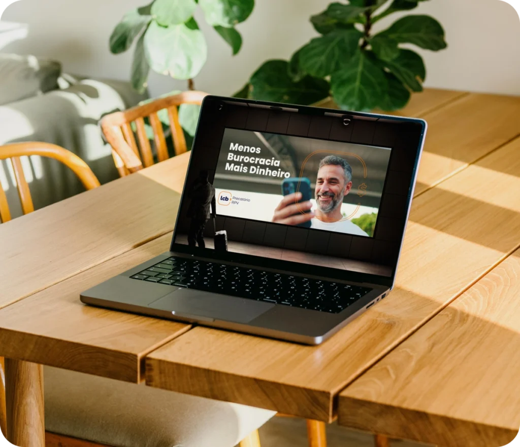 Laptop exibindo vídeo sobre "Menos Burocracia Mais Dinheiro" em mesa de madeira